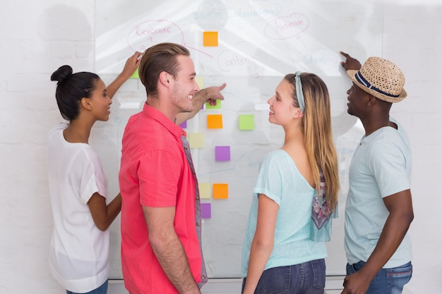 A group of students brainstorming ideas using sticky notes on a whiteboard in a brightly colored, collaborative workspace.