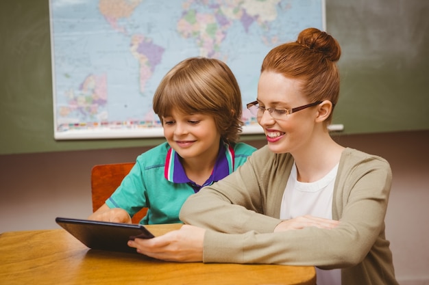 A middle school teacher sitting at a desk with a student, reviewing the student's individualized education plan (IEP) on a tablet. They are both smiling and engaged in the discussion.