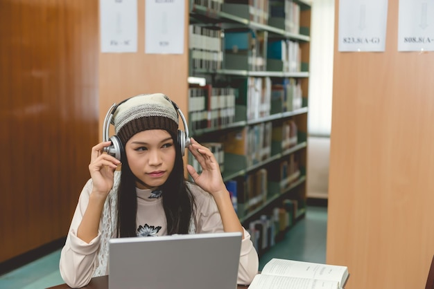 A high school student using speech-to-text software on a laptop in a library setting. The student looks focused and is wearing headphones.