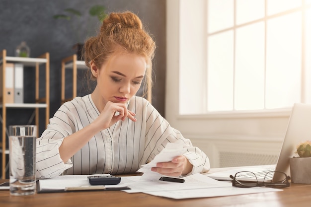 A person sitting at a desk, reviewing financial documents with a calculator nearby. The scene depicts the process of managing personal finances and exploring options for student loan repayment.