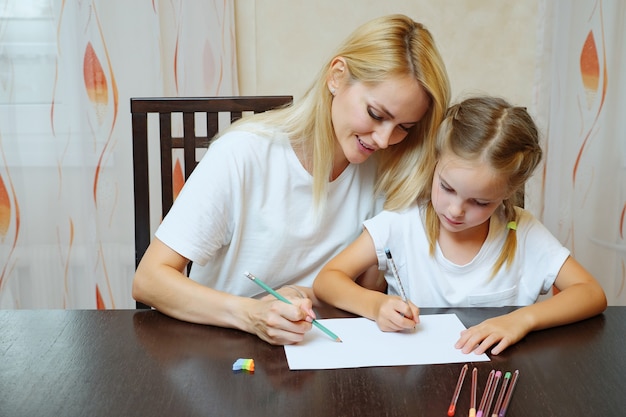 A mother is filling out an application form at a table, with a child sitting next to her drawing with crayons.