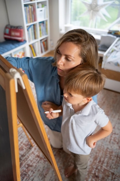 A close-up shot of a teacher interacting with a small child, with the teacher kneeling to be at eye level with the child. Both are smiling and engaged in a conversation, set in a colorful and inviting classroom. The focus is on the positive and supportive interaction between the teacher and the child.