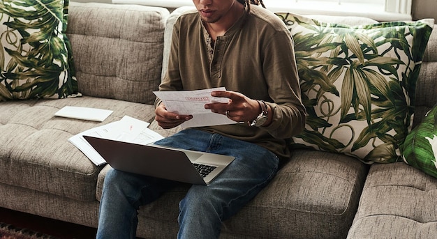 A homeowner sitting at a table, carefully reviewing documents and filling out a grant application form with a focused expression. A laptop is open nearby, displaying a government website.
