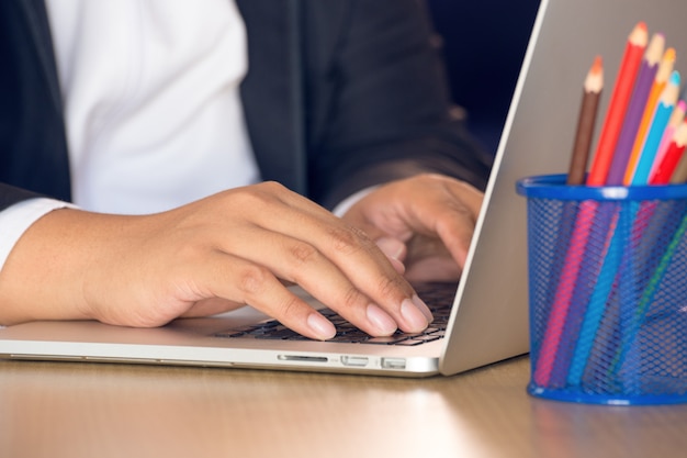 A close-up of a teacher's hands working on a laptop, focusing on the screen displaying information about the Public Service Loan Forgiveness (PSLF) program. The scene is set in a quiet classroom, highlighting the personal effort and research educators undertake to understand and apply for these programs